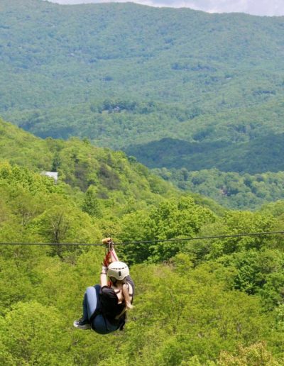 Person on zipline with NC mountains in background at ziplining park near Forest City, NC.