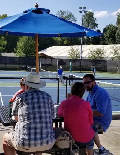 Spectators seated beneath umbrellas beside the Burlington City Park tennis courts.