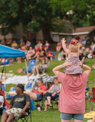 Child sitting on an adult's shoulders during a Burlington City Park event.