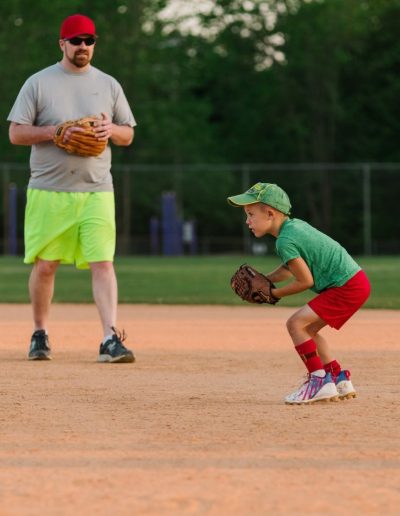 Young baseball player fielding beside a coach at Burlington City Park.