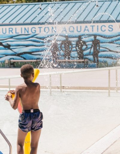 Boy playing among spray features outside Burlington Aquatics.