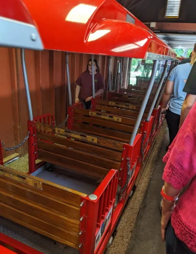 Passengers boarding a red train car at Burlington City Park.