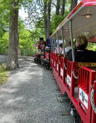 Passengers riding the red miniature train through Burlington City Park.